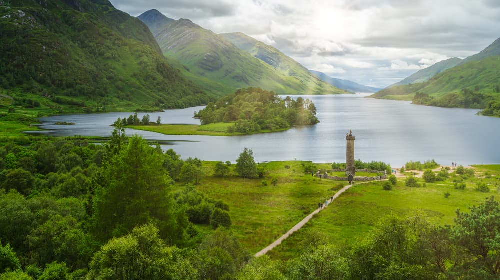 Aerial view of the Glenfinnan Monument on the shore of Loch Shiel, surrounded by green Highland hills
